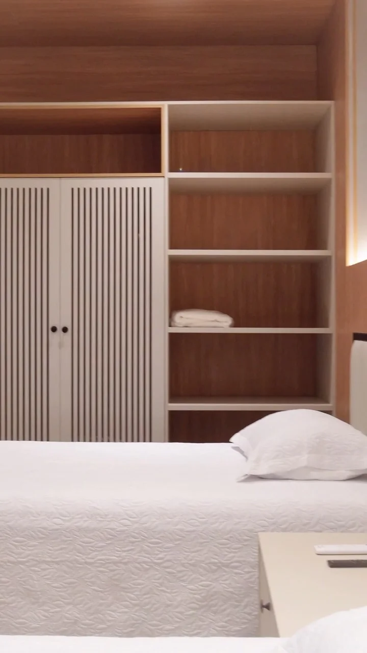 Dormitório com cama clara, painel ripado e iluminação indireta
